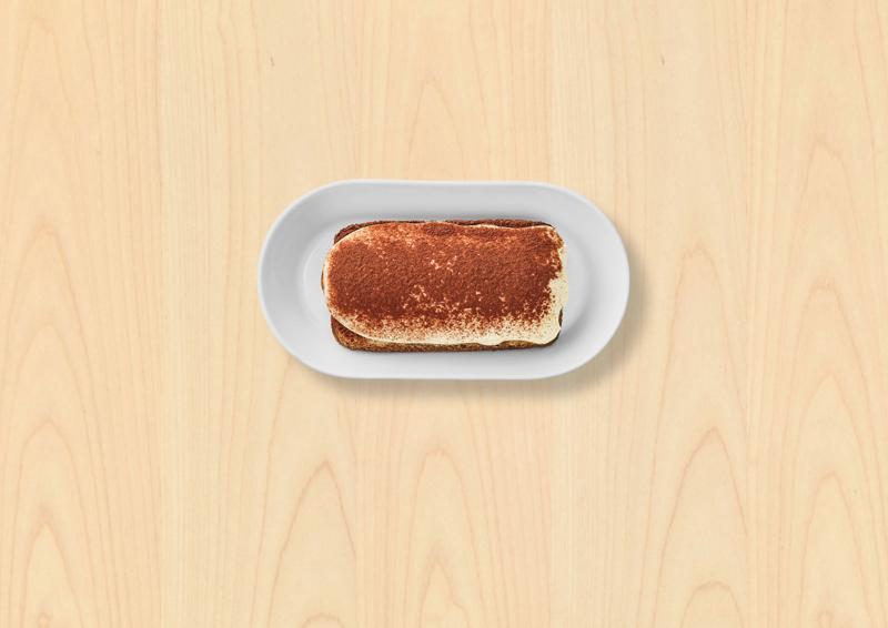 Un tiramisu au café dans une assiette blanche sur fond bois clair