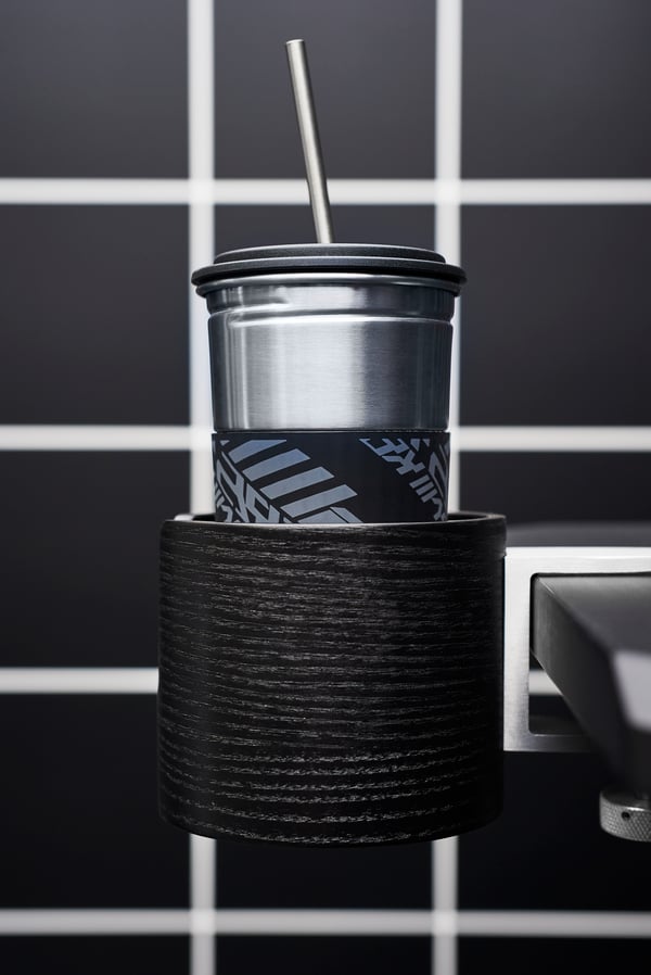 Mug with a lid and a straw holder attached to a computer gamer’s black desk with headphones in the blue background.