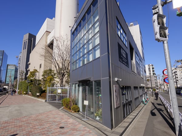 ガラス張りの建物が並ぶ都市の街角。青空の下、歩行者と自転車が行き交う現代的な街並み