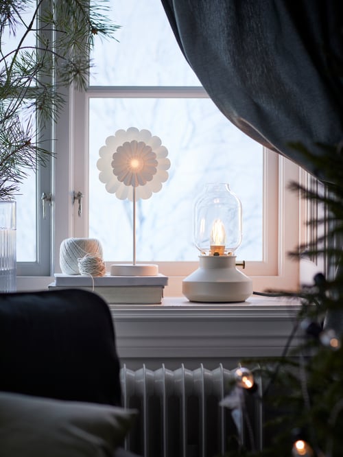 A windowsill with a beige TÄRNABY table lamp with a ROLLSBO dimmable LED bulb next to a STRÅLA LED table decoration.