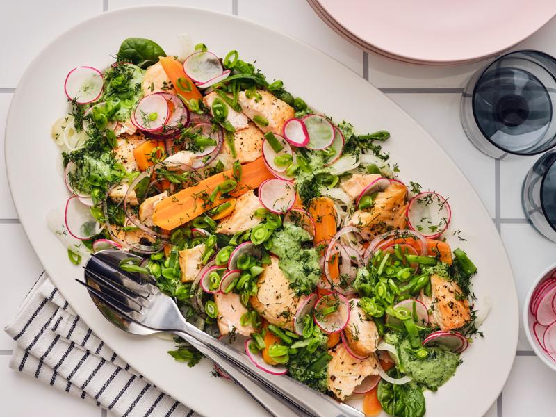 A colourful salad with grilled salmon, radishes, carrots, snap peas, and fresh herbs, served on a white plate.