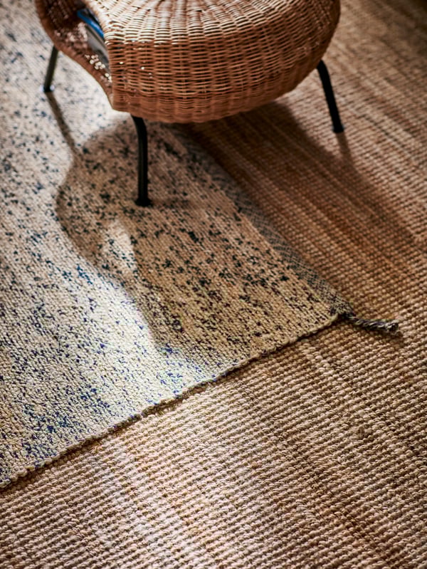A large jute rug and a smaller jute rug with dark blue wool randomly woven into the jute and a rattan footstool.
