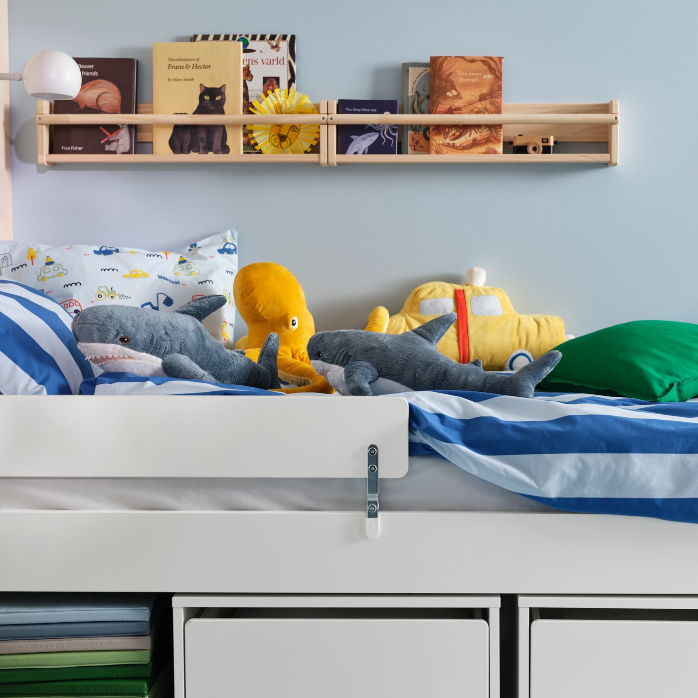 A SLÄKT child’s bed with a BARNDRÖM duvet cover and BLÅVINGAD soft toys. A PLUFSIG gym mat below, a FLISAT wall shelf above.
