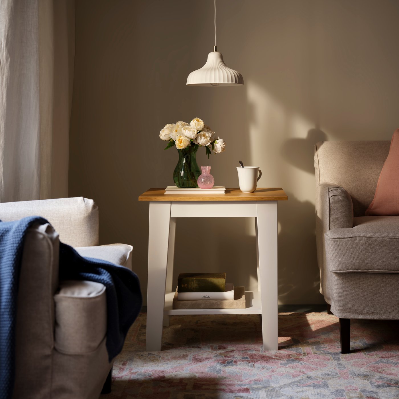 Obývací pokoj s pohovkou, židlí a bílým odkládacím stolkem ÄMMARYD, na kterém je váza s květinami a šálek čaje.