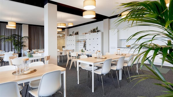 Blick in eine Büro-Küche mit weisser Küchenzeile und Esstischen, auf denen Karaffen und Gläser stehen.