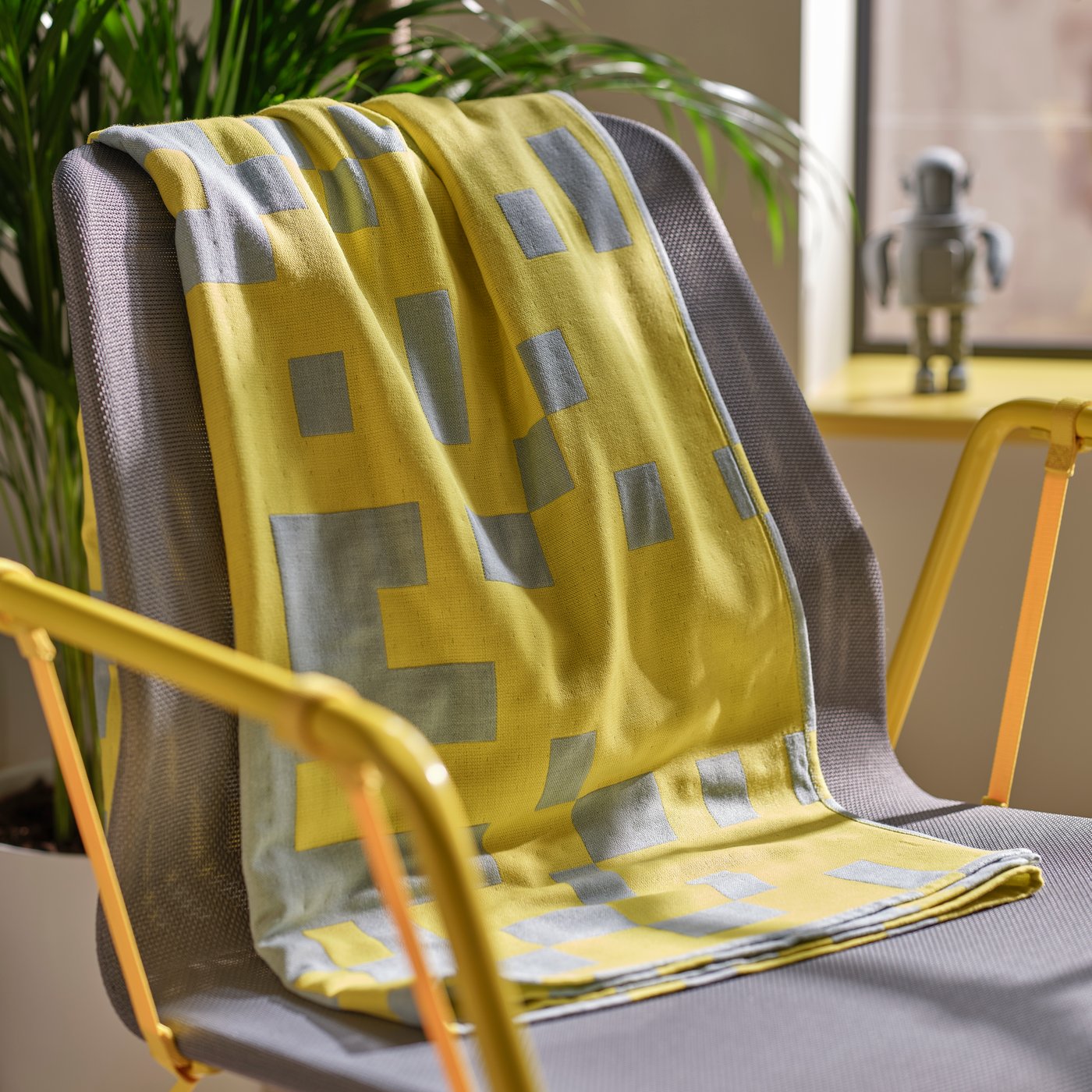 A BRÄNNBOLL throw in pale blue/bright yellow is draped over the back of a BRÄNNBOLL gaming easy chair in grey/bright yellow.