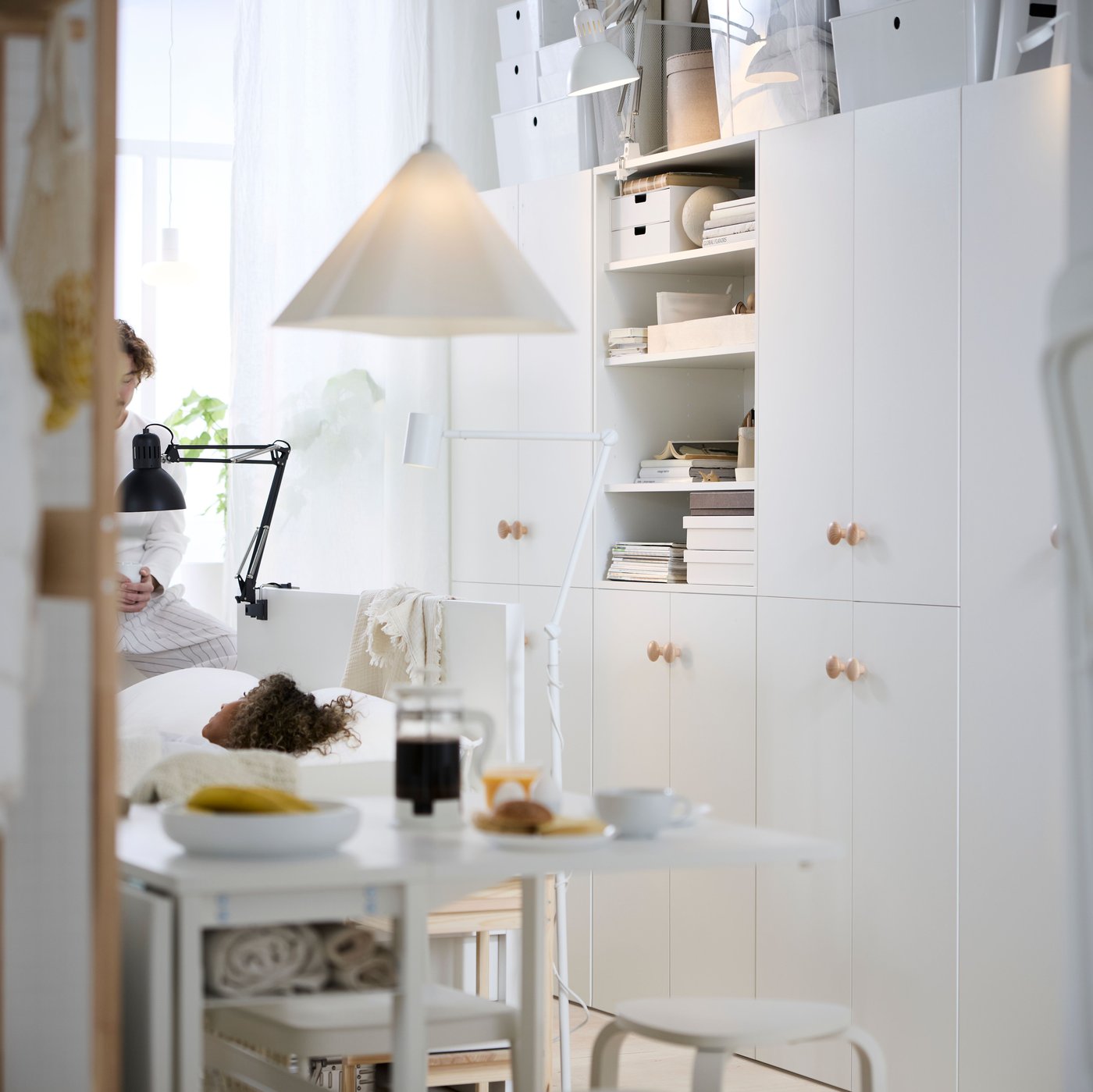 A multifunctional living space with white LASTARE cabinets, a white bed frame and white VIHALS table set with breakfast.