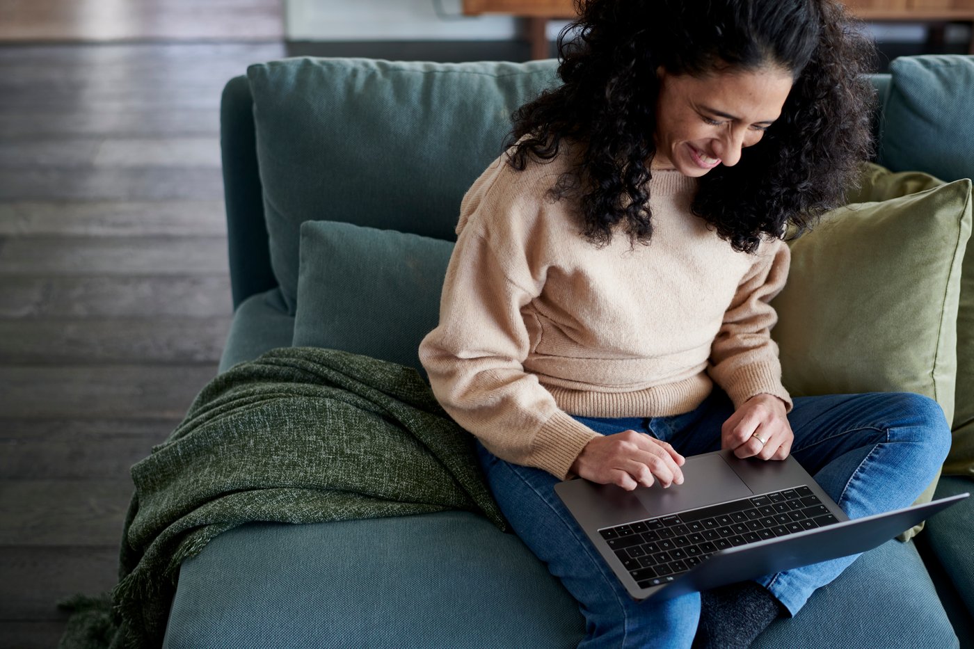 A woman sits on a sofa with a laptop on her lap