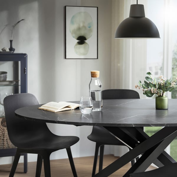 A black round MARIEDAMM dining table surrounded by black dining chairs and a black ceiling lamp.