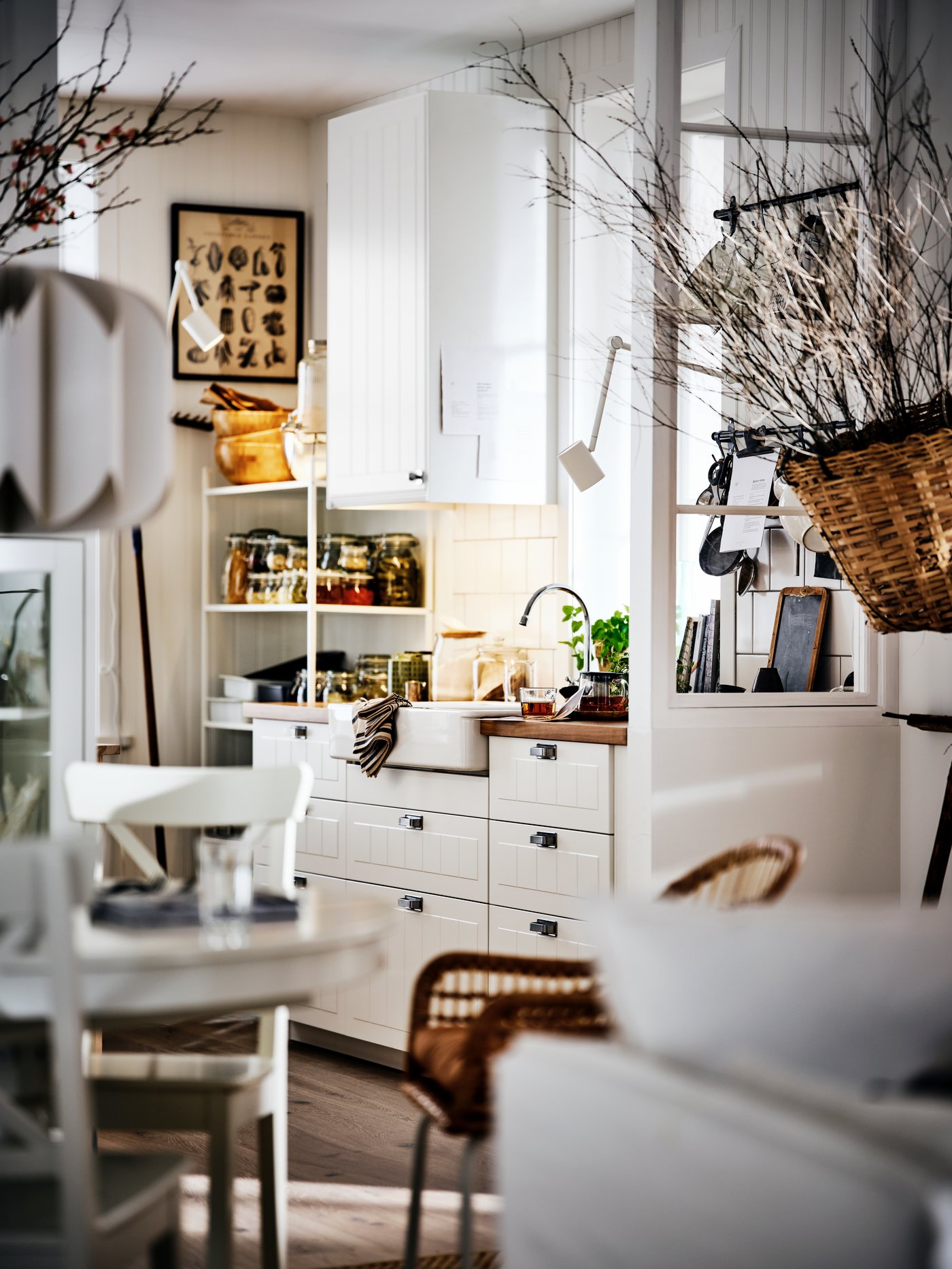 Dapur dan ruang makan gaya desa, dengan kabinet berwarna putih, dan bahagian atas kaunter kayu serta dahan kering hiasan.