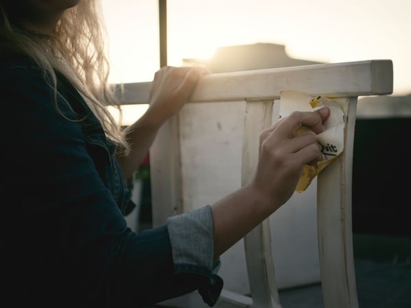 A person’s hands are shown using a yellow sponge to clean a white surface, with sunlight filtering through in the background. The image suggests a theme of cleanliness, care, and sustainability. The word “huit” appears in the image, possibly as part of a larger, unseen context.