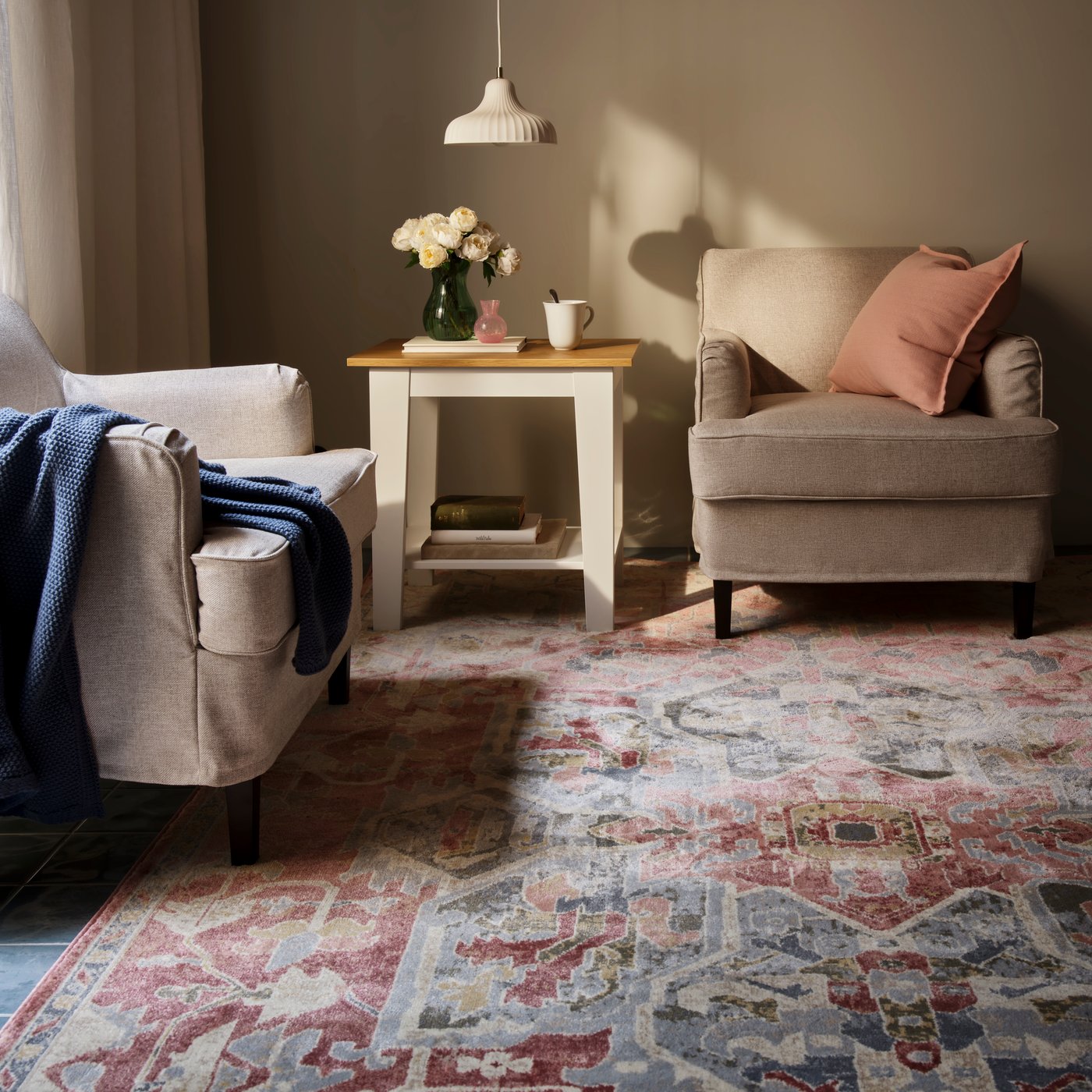 A living room with a pink-beige, ornamental-pattern JÄRNVÄG low-pile rug placed beneath two chairs and a table.