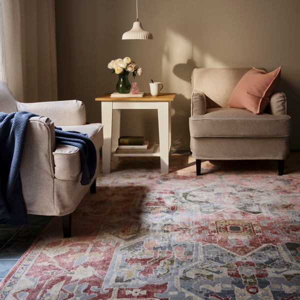 A living room with a pink-beige, ornamental-pattern JÄRNVÄG low-pile rug placed beneath two chairs and a table.