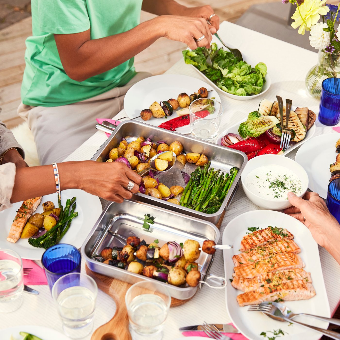 A group of people serve themselves SJÖRAPPORT salmon fillets, roasted potatoes and vegetables from IKEA 365+ serving plates.