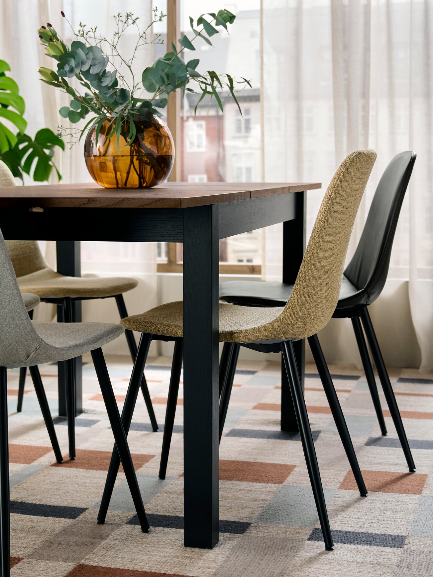 NORDMANSSKÄR fully upholstered chairs in different colours are placed around a square dining table in a bright dining room.