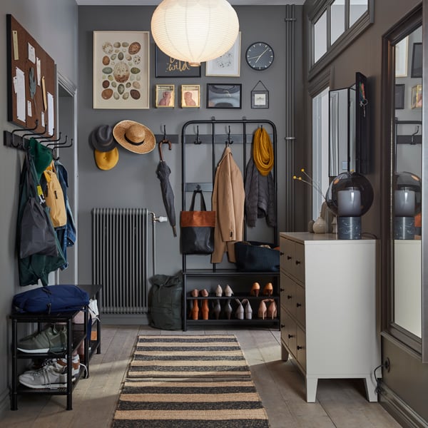 A hallway with a PINNIG coat rack, shoe bench and hook rack on two sides of the space holding coats, hats, bags and shoes.