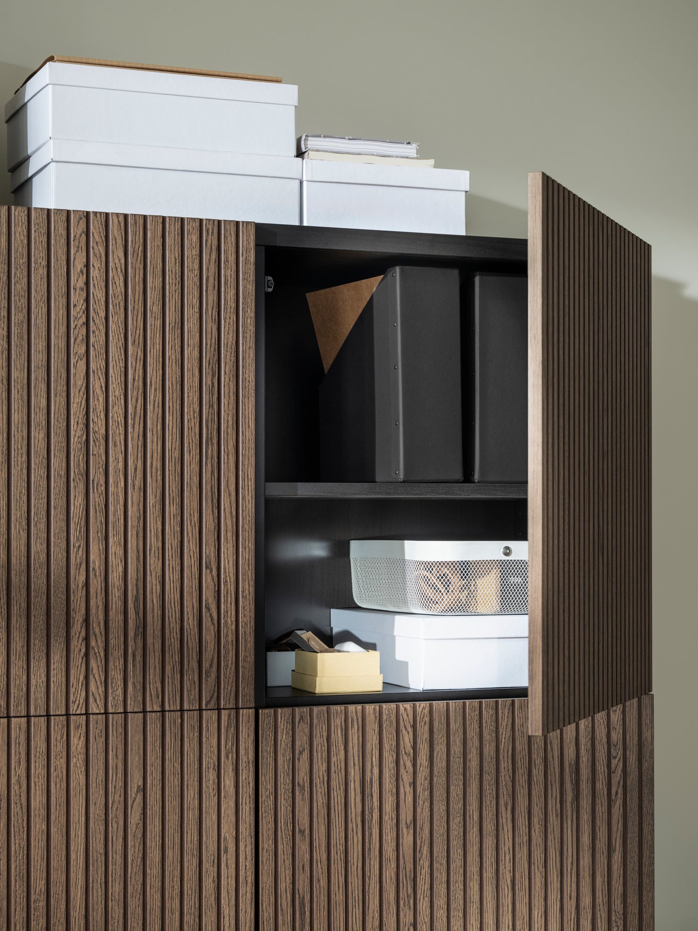 White TJENA storage boxes in and on top of black-brown BESTÅ cabinets with brown-stained oak-veneer BJÖRKÖVIKEN doors.