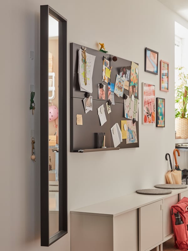 A black mirror with hinges revealing hooks with keys hanging on them behind. A memo board with drawing and pictures.