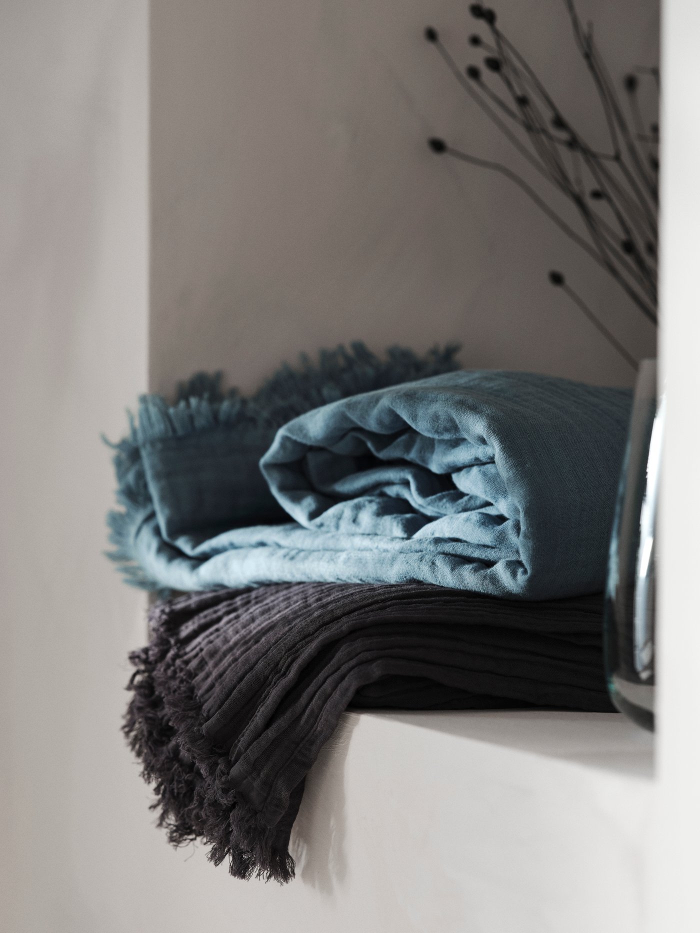 Dos mantas VALLKRASSING en un rincón, junto a un jarrón de vidrio.