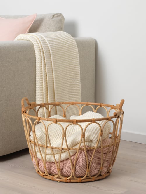 Living room with a round basket placed on the floor, fabrics and home textiles, a white throw, a sofa, a cushion cover.