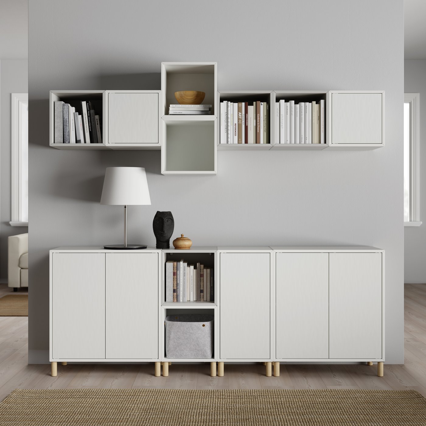 Minimalistisches Wohnzimmer mit weißen Hänge- und Unterschränken, dekoriert mit Büchern, Lampe und Keramikobjekten vor grauer Wand.