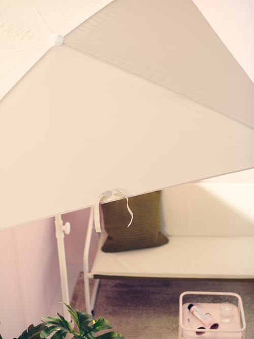 Un parasol TVETÖ blanc projette de l’ombre sur un canapé extérieur à deux places INGMARSÖ blanc sur un balcon urbain moderne.