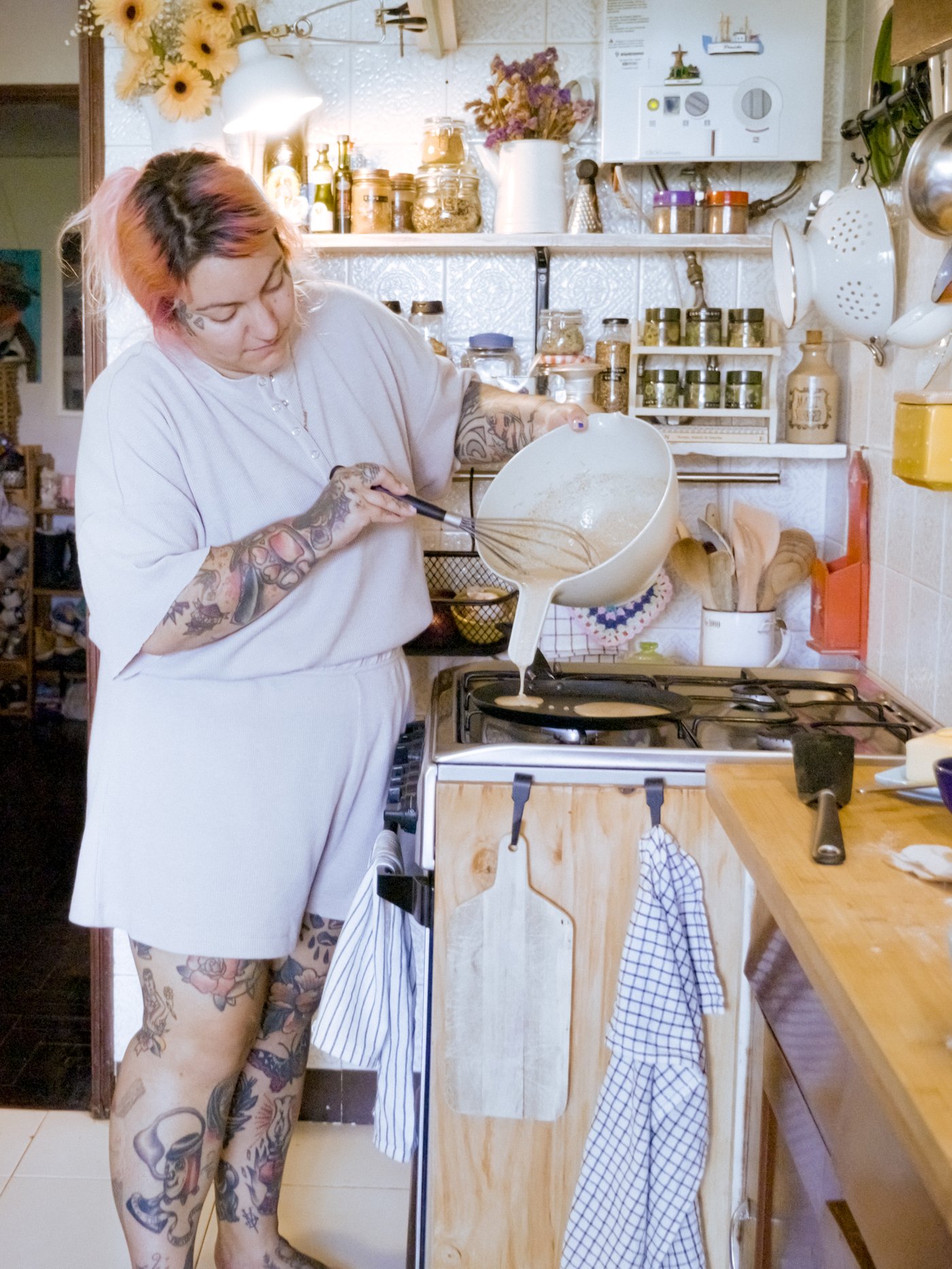 A woman pours pancake mix from a VISPNING mixing bowl into a HEMLAGAD pancake pan on a stove.