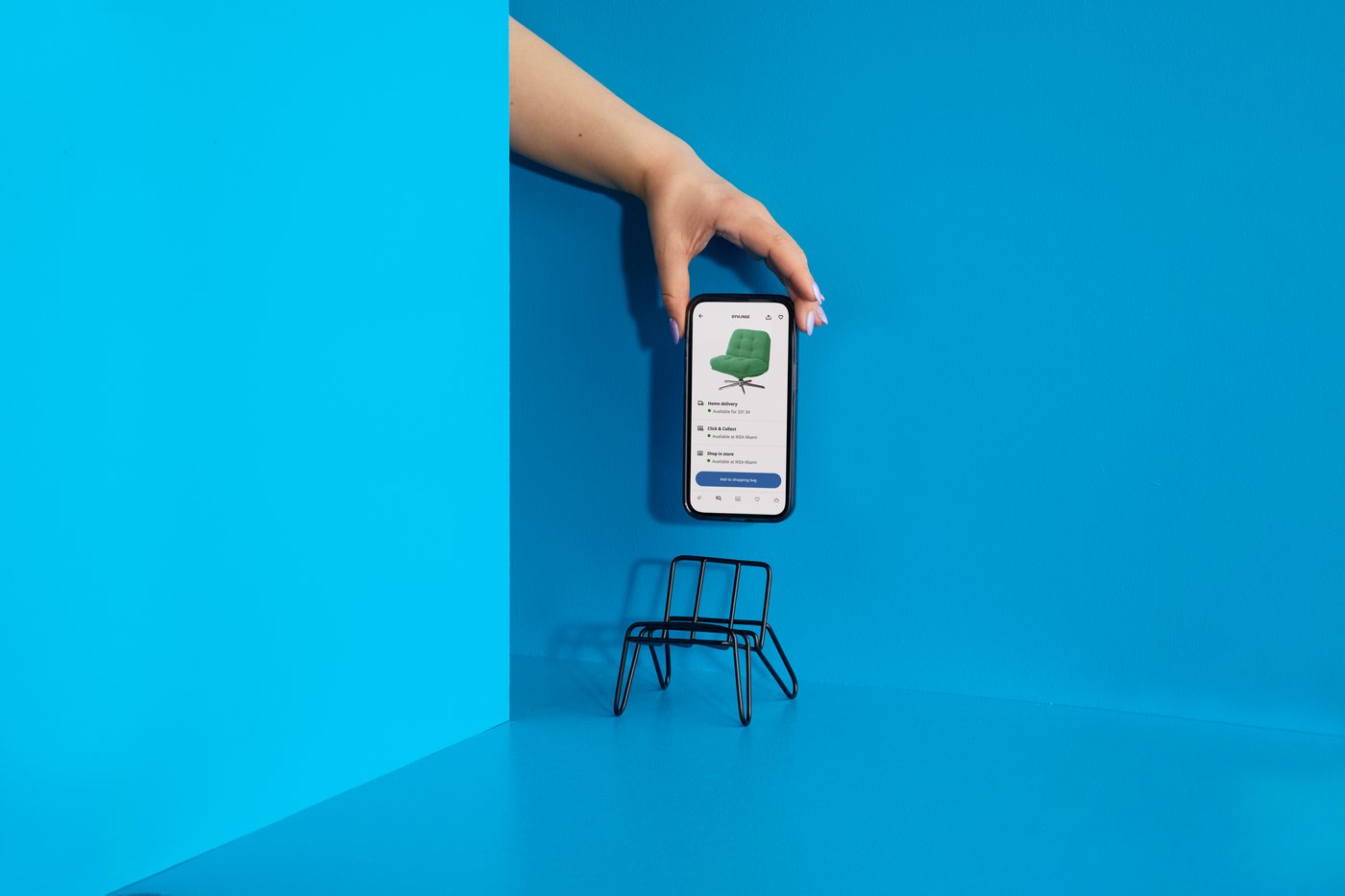 ruka s telefonem na modrém pozadí, s malou židlí na telefon. 