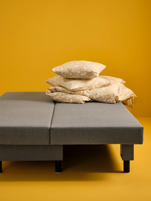 Ein graubeiges ÄLVDALEN 3er-Bettsofa in Bettfunktion in einem Raum mit gelben Wänden. Darauf liegt Bettwäsche in JÄTTEVALLMO Bettwäsche.