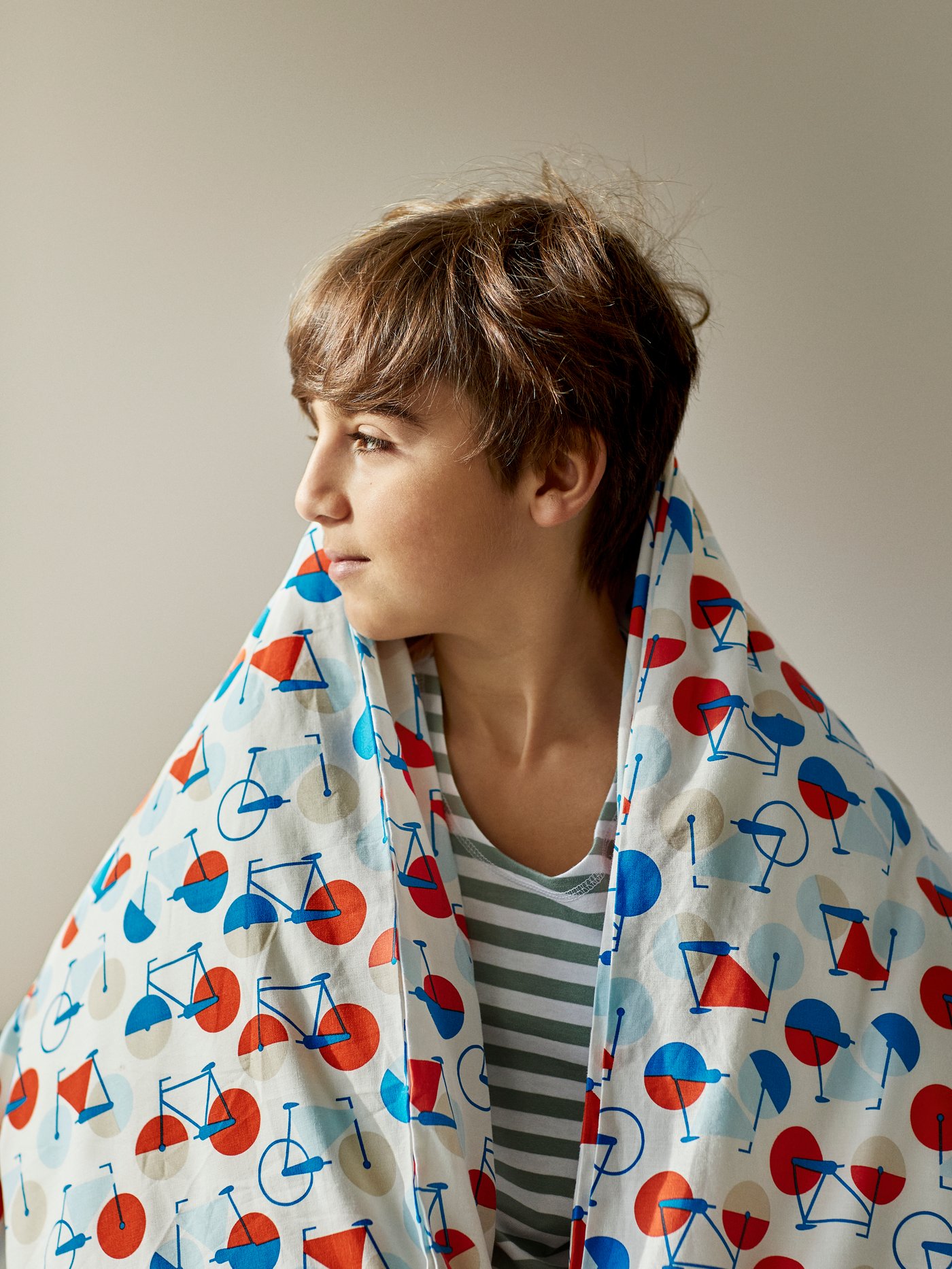 A young boy is wrapped in a SPORTSLIG covered quilt and is looking towards the left.