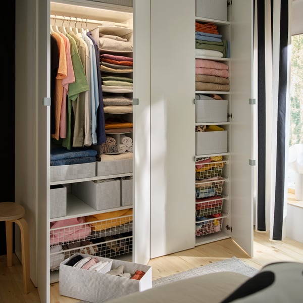 LASTARE wardrobe combination with hanging clothes, folded textiles and STUK storage boxes and baskets in a bright bedroom.