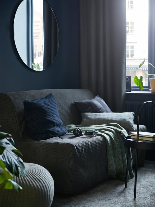 Living room with a standard 2 seat sofa bed with removable mattress and sofa cover, placed next to a pouffe and a side table.
