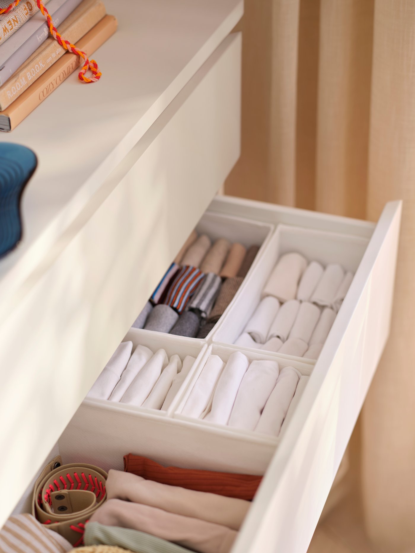 An extended drawer of an off-white TONSTAD chest of drawers with white SKUBB boxes with various things organised in them.