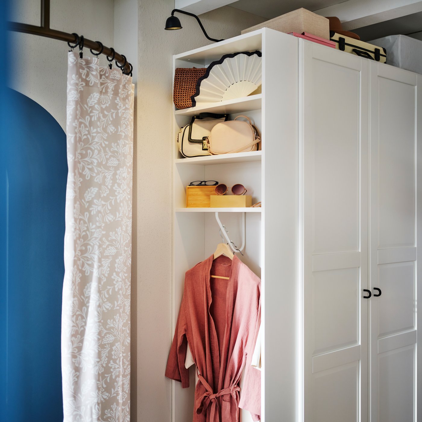 A white PAX/TYSSEDAL wardrobe combination in a bedroom with the end unit holding a dressing gown, handbags and accessories.