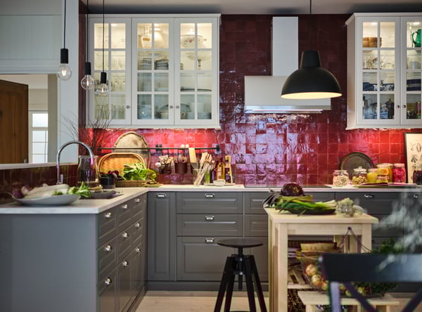 Produce and utensils dot a red-tiled kitchen with white wall cabinets, a white marble effect worktop, and grey base cabinets.