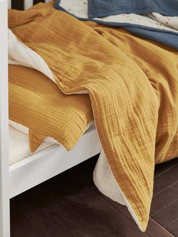 Close up of the yellow GULDVÄVARE 3-piece bedlinen set in a white cot.