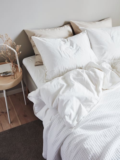 Chambre à coucher avec housse de couette blanche et 2 taies d’oreiller en coton recouvertes d’un couvre-lit blanc.