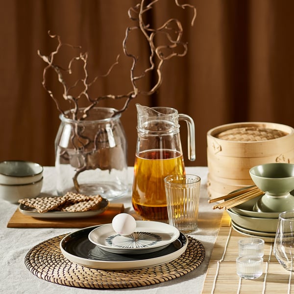 Ein gedeckter Tisch mit Wasserkrug, verschiedenen Tellern und anderer Auswahl an Geschirr und Tischsets aus der IKEA LÄTTAD Serie.