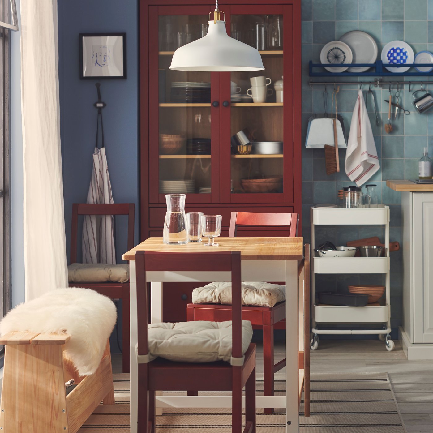 Bredvid ett stort fönster - ett litet bord för två med vita ben och en ljusbrun träskiva och två röda stolar.