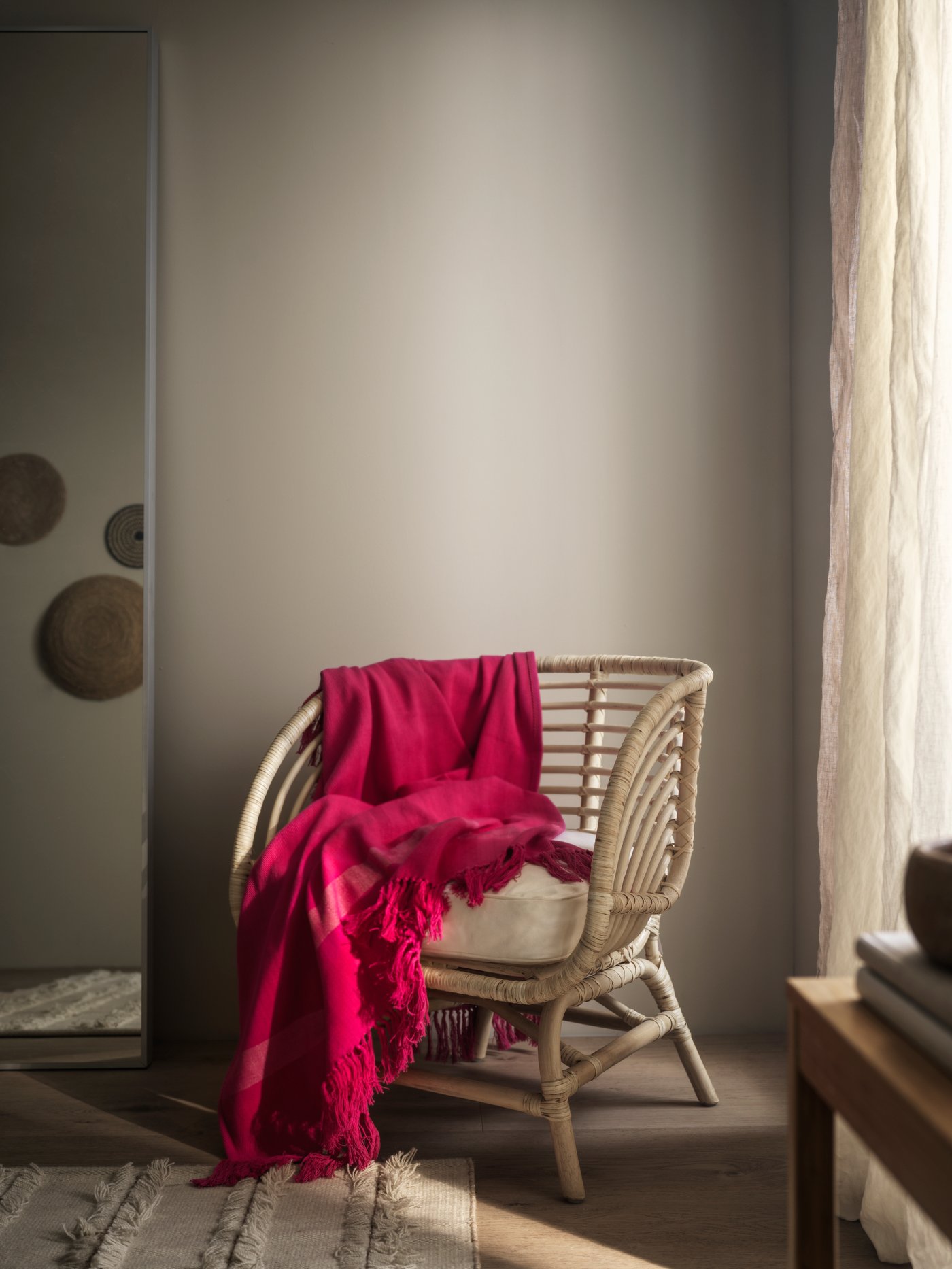Set in a cosy warmly lit corner of a room, the handmade HILLEGÄRD throw is draped on a natural material chair.