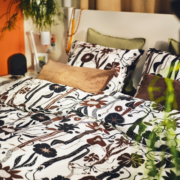 An off-white TONSTAD bed covered in white/black/brown LUNDSKAFTING bed linen with cushions in green and brown covers.