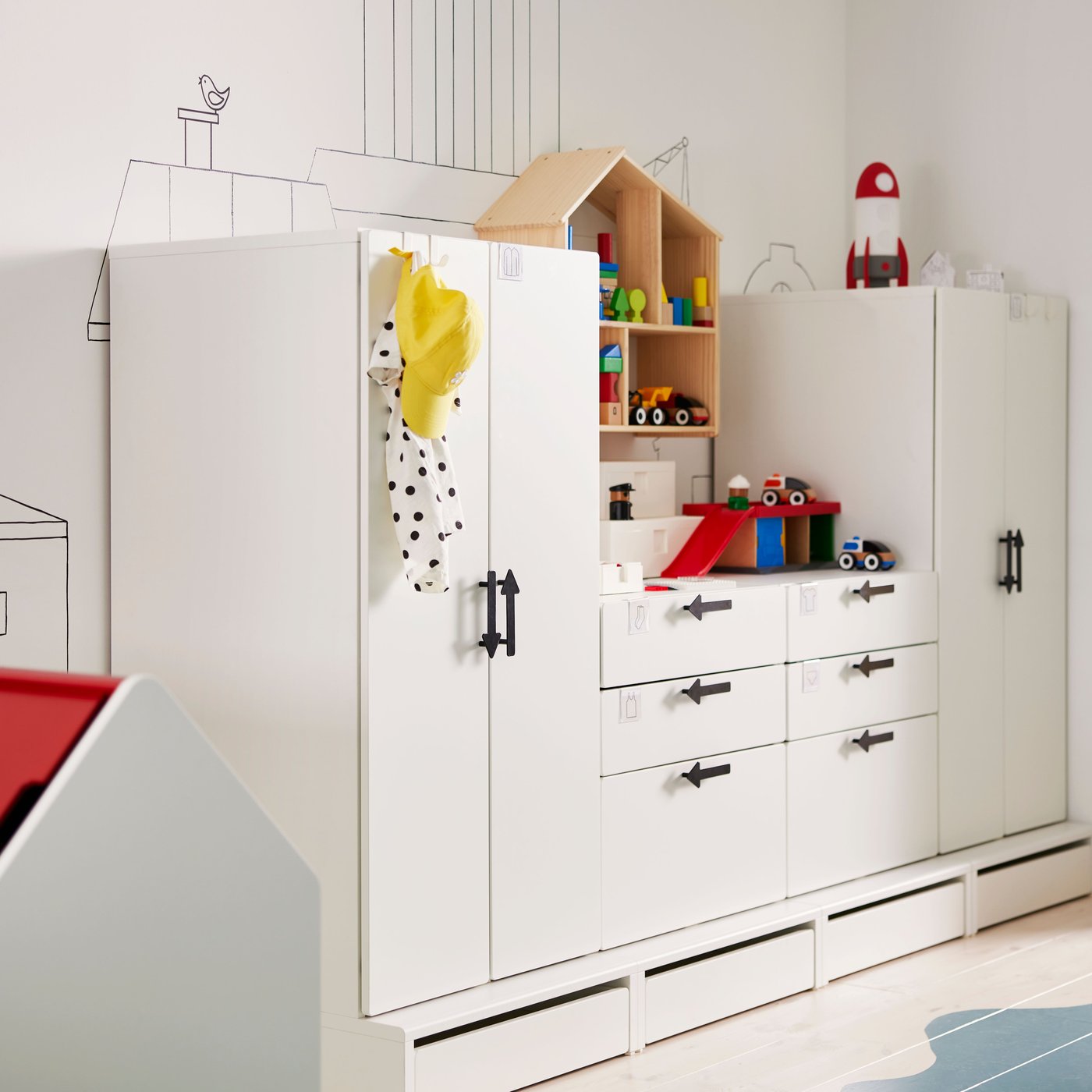 White storage unit in different heights along a wall with painted decorations on it. Blue sea painted on floor.