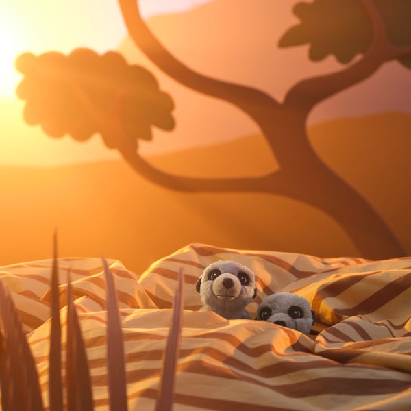Deux peluches suricate au milieu d’une housse de couette rayée, dans un paysage de savane ensoleillé.