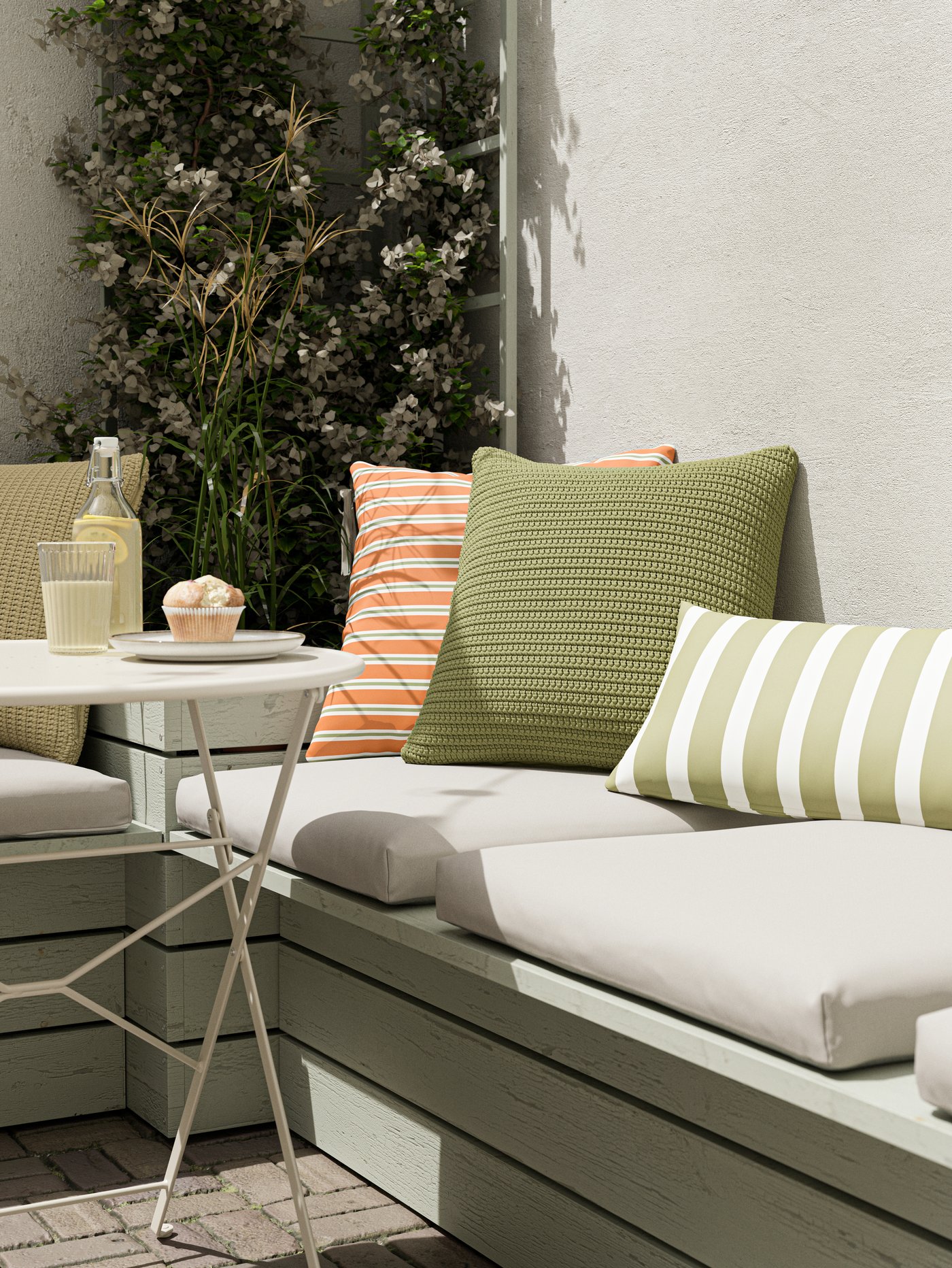 حافة للجلوس عليها وسائد بيج ووسائد خضراء وبرتقالية وطاولة عليها كب كيك وعصير ليمون.