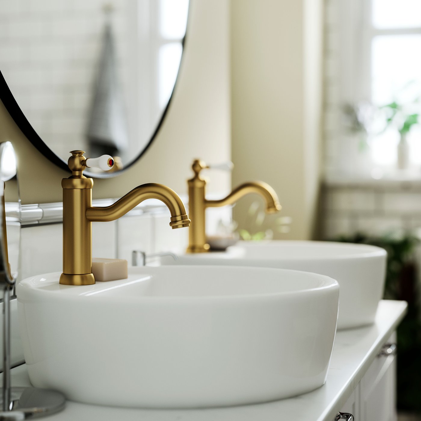 Two HAMNSKÄR sink mixer taps in brass colour on white basins with a round mirror and light decor.