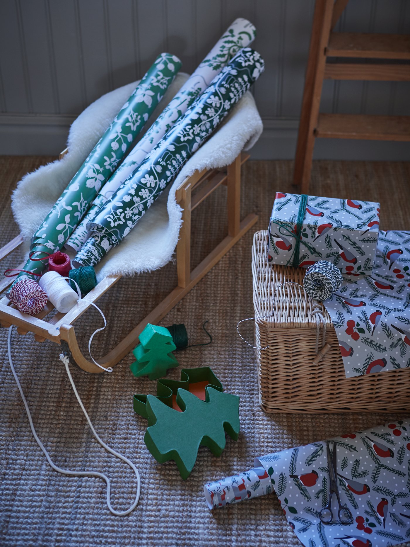 Regalos envueltos en un rollo de papel de regalo verde VINTERFINT con estampado de animales; a su lado hay rollos de papel de regalo y cordeles.