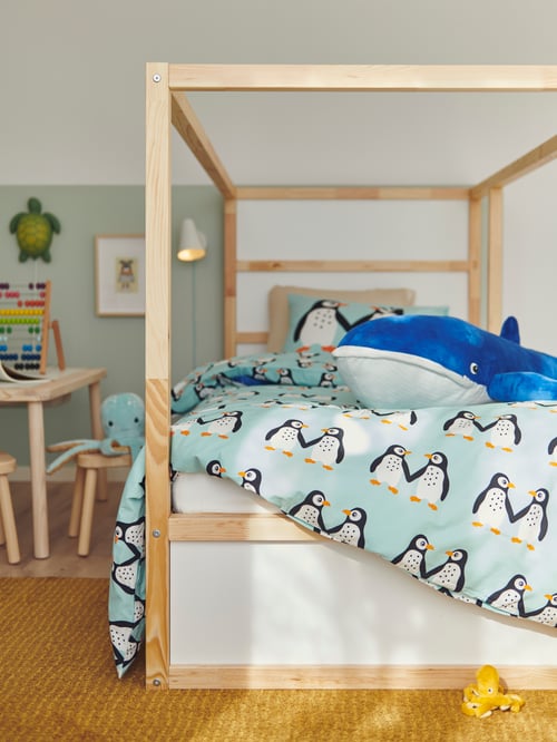 Bedroom area with a reversible bet, a duvet set, a toy whale, a low pile rug, a turtle-shaped wall lamp, a stool and table.