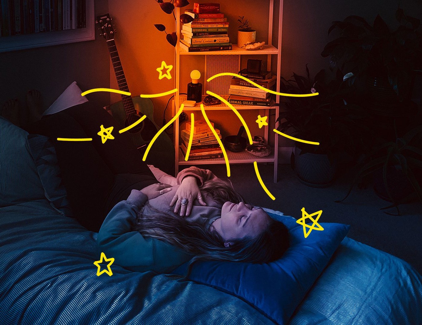 A woman lying on her bed, meditating, in a room illuminated by an orange-coloured light.