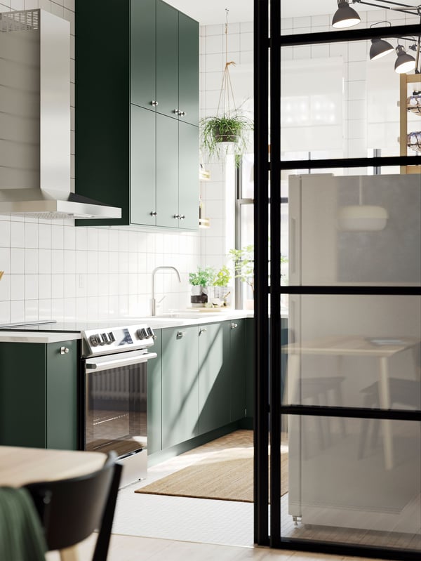 A wide doorway into a kitchen with deep green HAVSTORP kitchen fronts and a white marble effect/laminate EKBACKEN countertop.