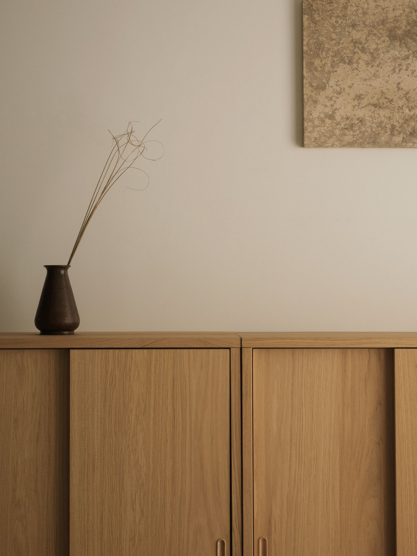 キャビネットは明るい木目で、その上には焦げ茶の花瓶がある。